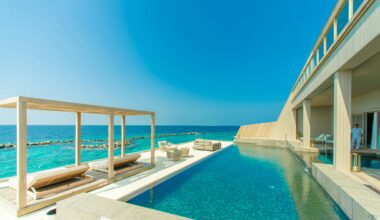 a swimming pool with lounge chairs and a deck on a beach