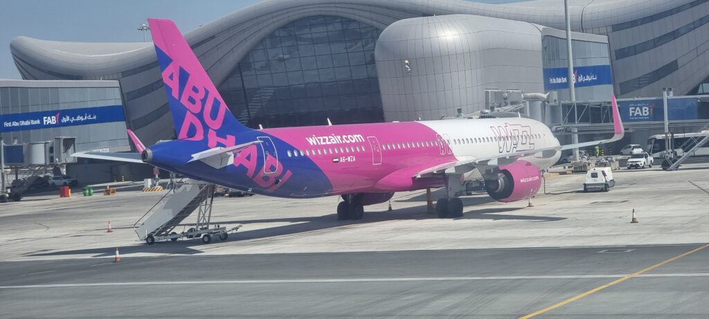 a pink and blue airplane in front of a building Wizz air fuel efficient aircraft