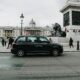 a black car on a street with a statue in front of it