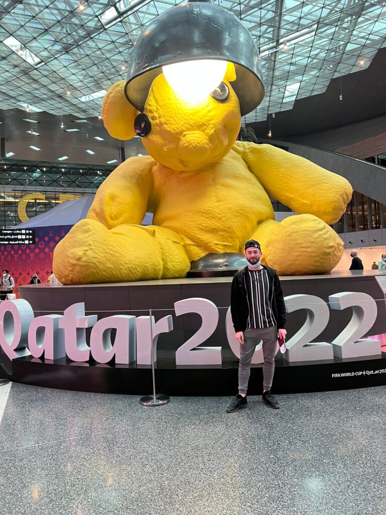 a man standing in front of a large yellow stuffed bear airport architecture